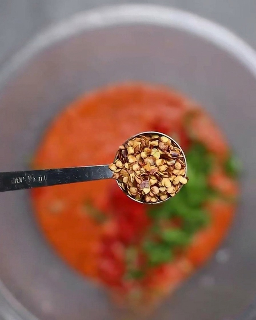 Dodawanie nasion chili do miski z bazą chili i posiekanymi papryczkami.