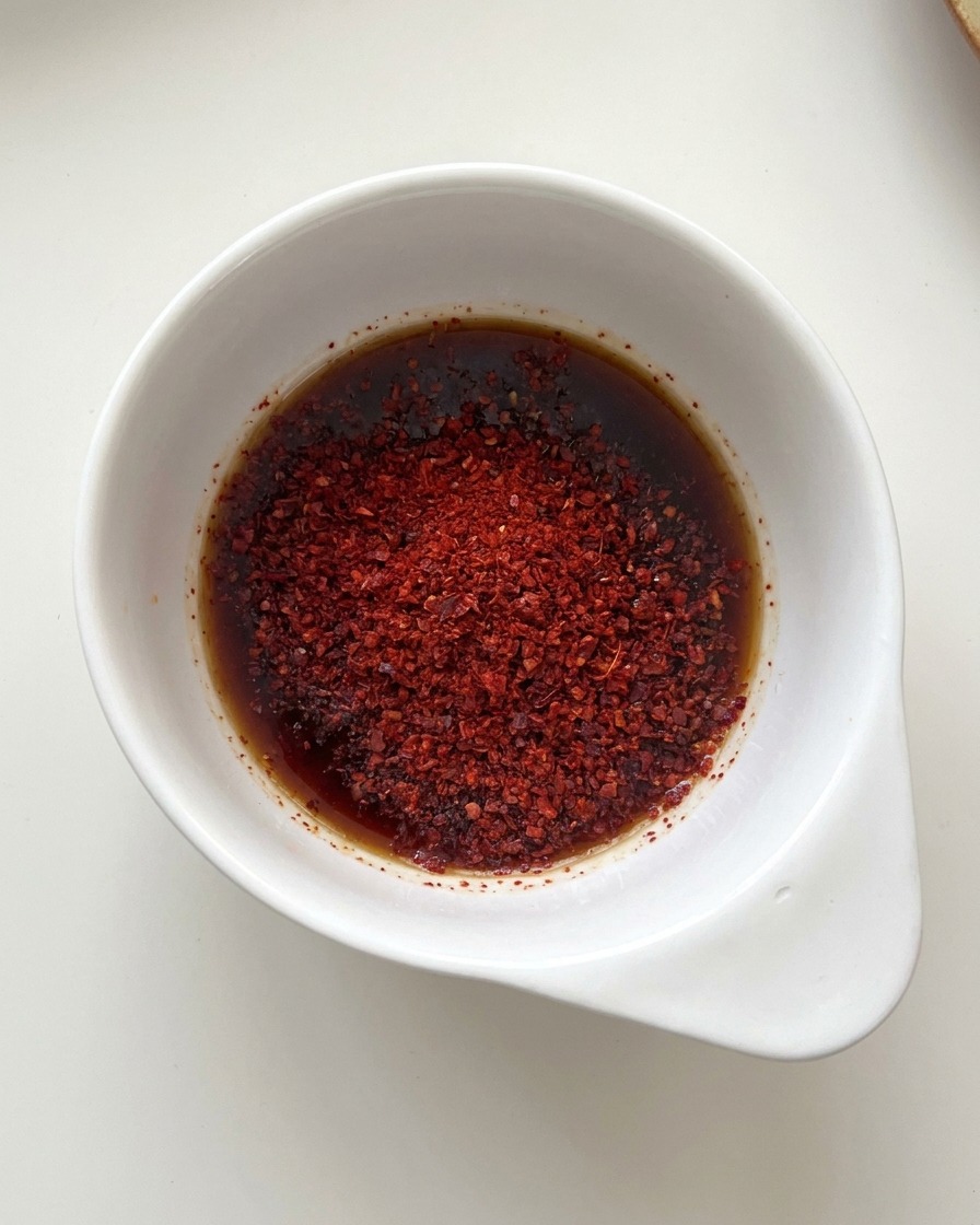 Mała biała miseczka z mieszanką sosu sojowego i jaskrawoczerwonego chili w proszku.