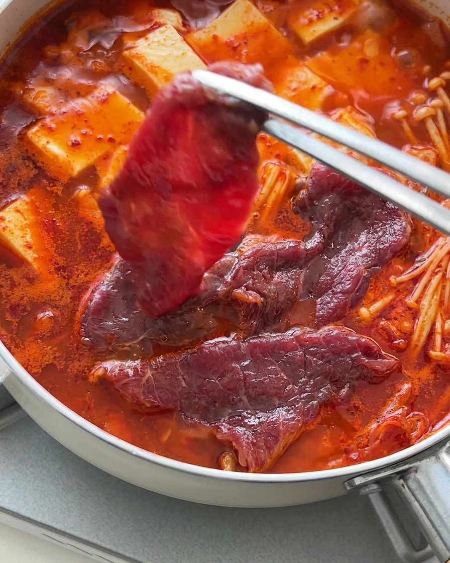 Szczypce układające cienkie plastry surowej wołowiny na wierzchu gorącej zupy z tofu.