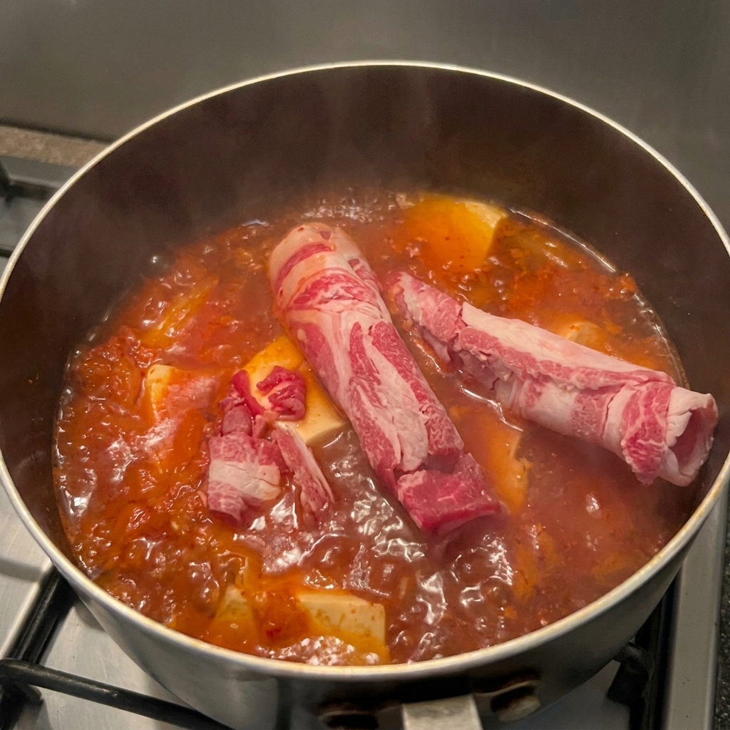 Cienkie plasterki surowej, marmurkowatej wołowiny wkładane do garnka z gotującą się zupą kimchi i tofu.