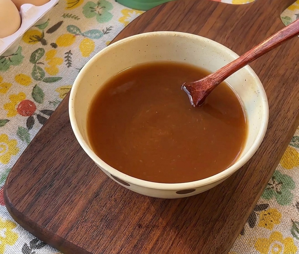 Drewniana łyżka mieszająca brązowy sos w małej ceramicznej misce.