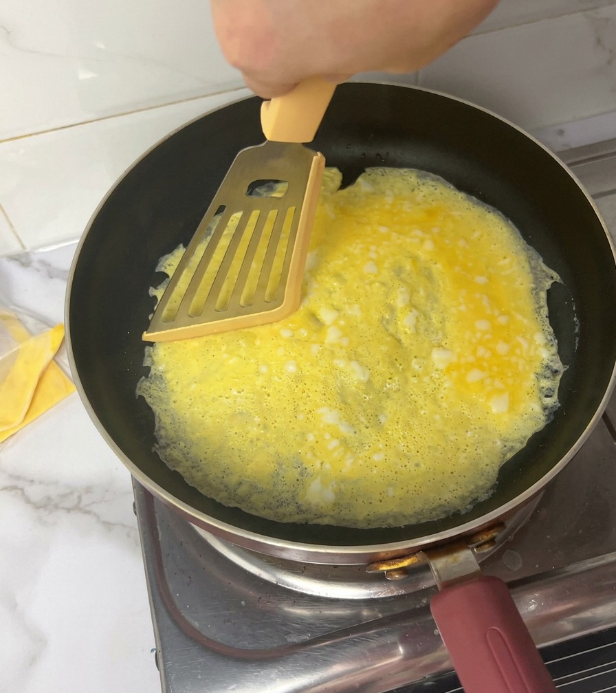 Ręka używająca żółtej łopatki do podzielenia cienkiego omletu na cztery części na patelni.