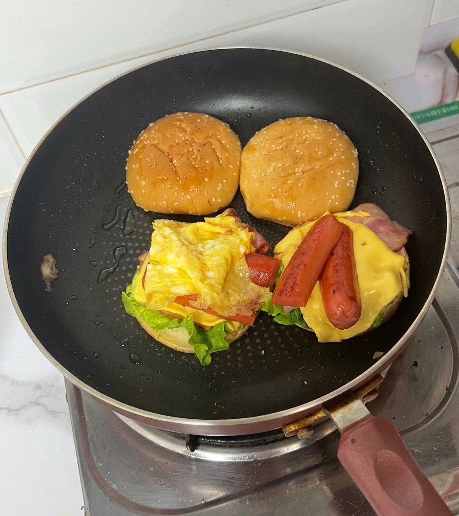 Złożony burger śniadaniowy na patelni z widocznymi wszystkimi warstwami.
