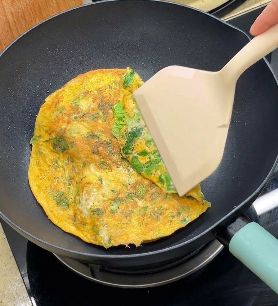 Łopatka zawijająca brzegi okrągłego omletu na połówki bułek na patelni.