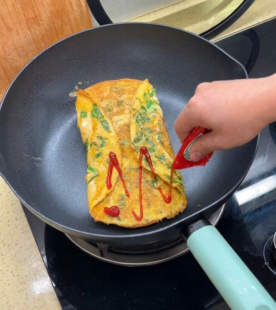 Ketchup wyciskany na złocisty omlet na patelni.