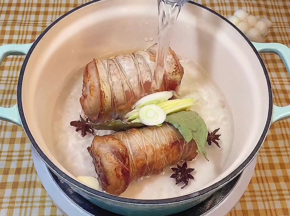 Wlewanie czystej wody do garnka z podsmażonym boczkiem, aromatami i przyprawami.