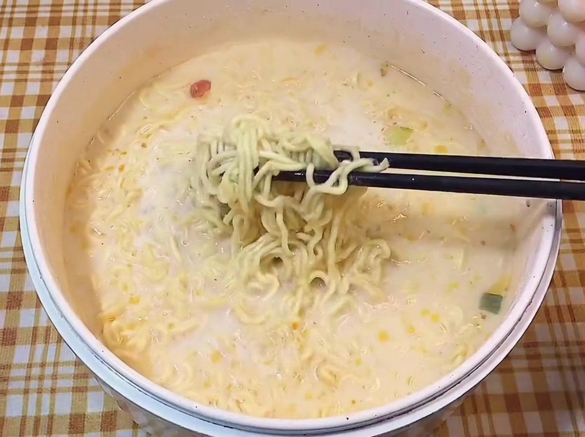 Czarne pałeczki wyciągające porcję ugotowanego, falistego makaronu ramen z mlecznego wywaru.