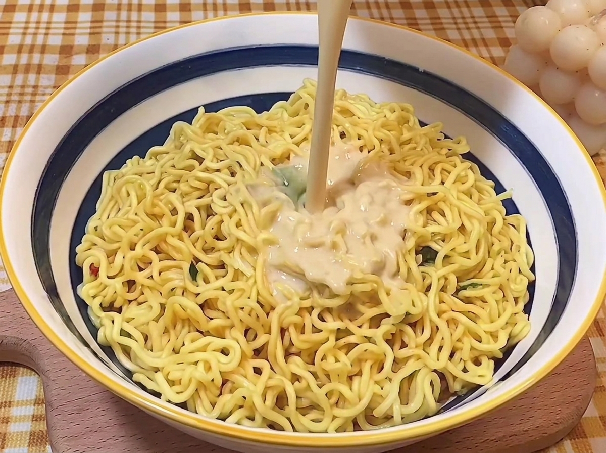 Strumień kremowego, bogatego wywaru tonkotsu wlewany na makaron w misce.