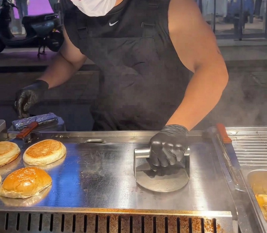 Ciężka metalowa praska dociskająca kotlet wołowy do gorącej płyty grillowej.
