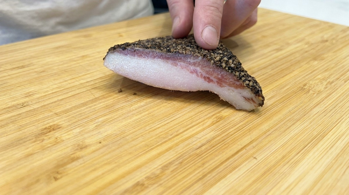 Kawałek guanciale w pieprzu na drewnianej desce do krojenia.