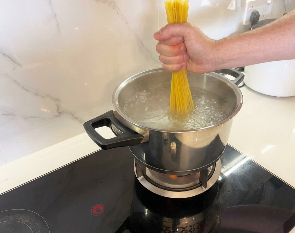 Wkładanie porcji suchego makaronu spaghetti do wrzątku.