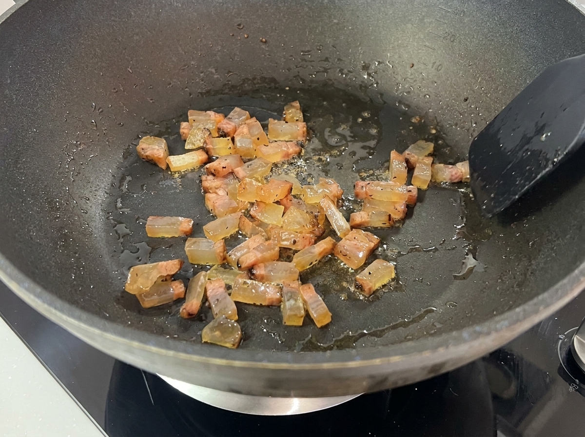 Smażące się kawałki guanciale we własnym tłuszczu na patelni.