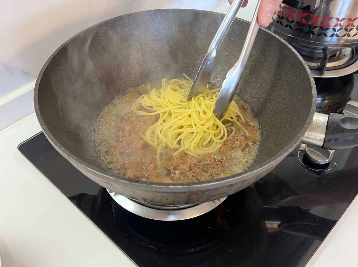 Przenoszenie ugotowanego spaghetti szczypcami bezpośrednio do patelni z mięsem.