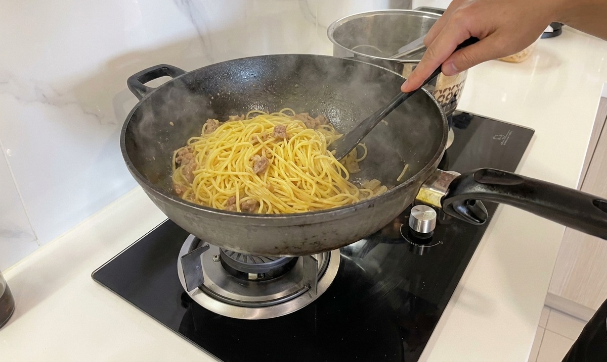Energiczne mieszanie spaghetti na patelni w celu uzyskania kremowego sosu.