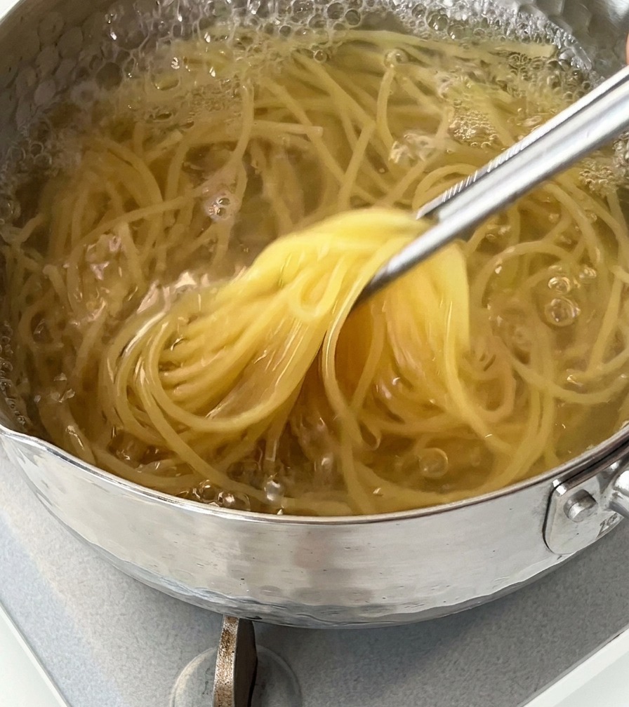 Zbliżenie na makaron spaghetti wyjmowany metalowymi szczypcami z garnka z wrzącą wodą.
