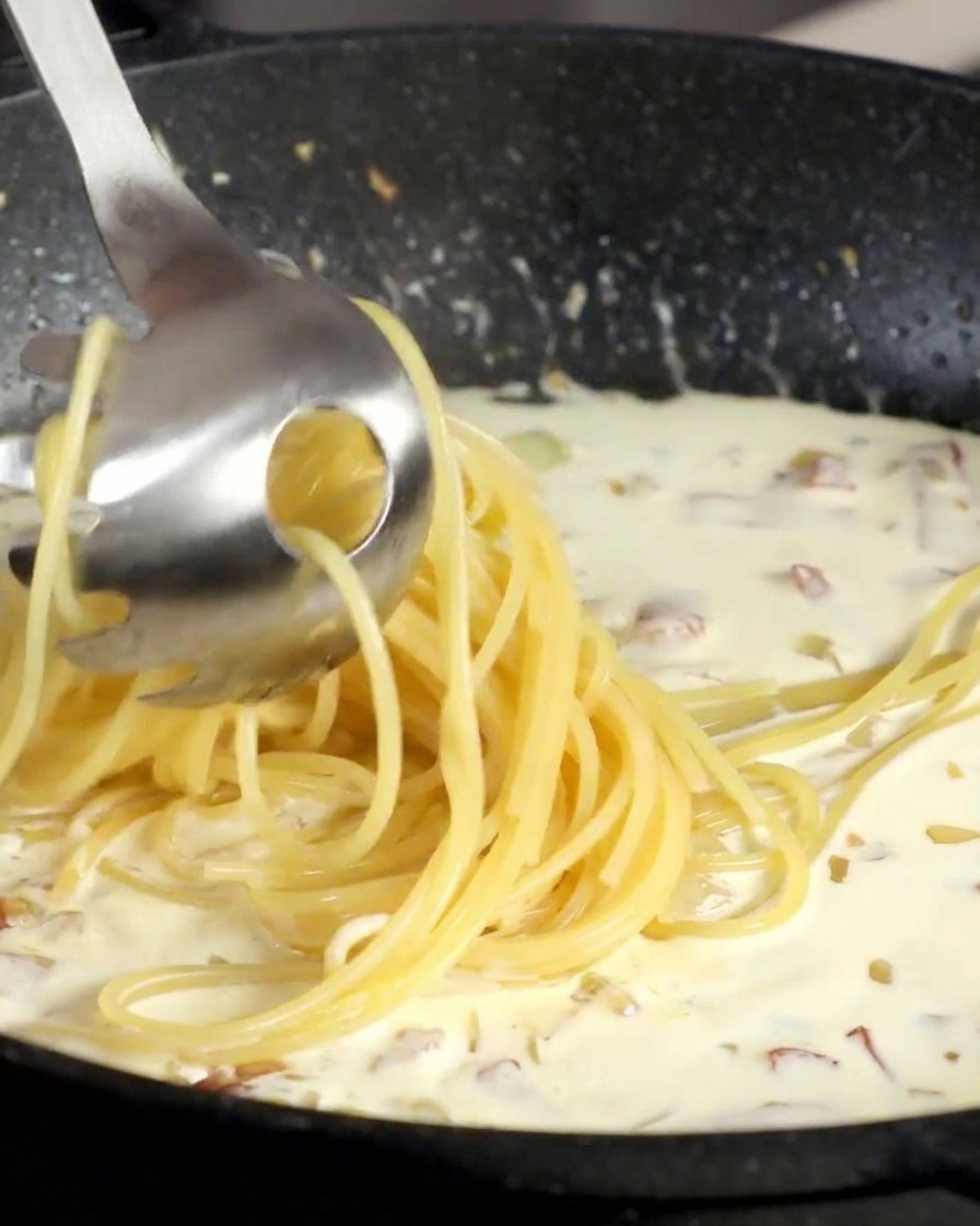 Widelec do makaronu przekładający spaghetti prosto do gotującego się białego sosu.