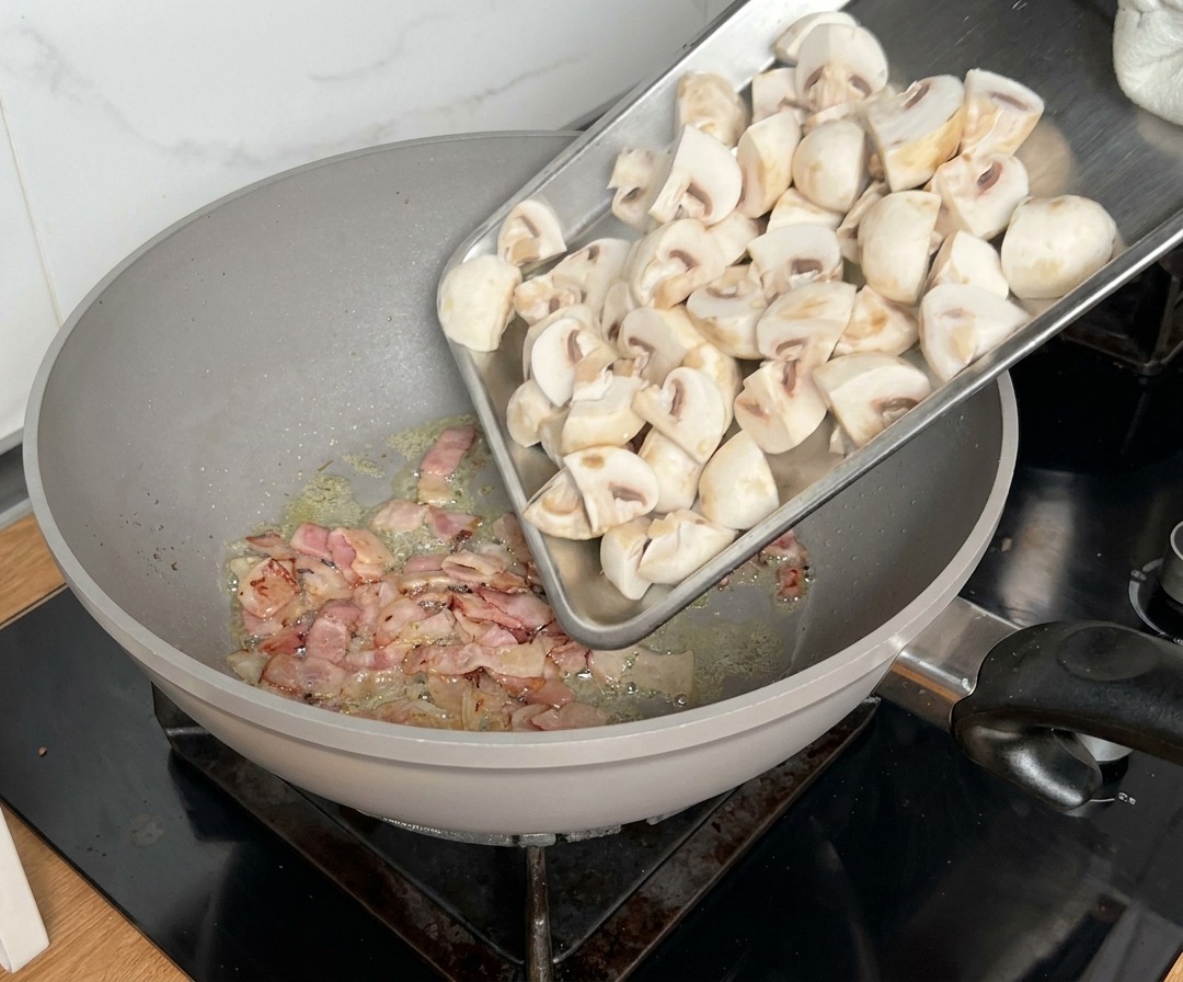 Ćwiartki pieczarek dodawane na patelnię, na której smaży się już boczek.