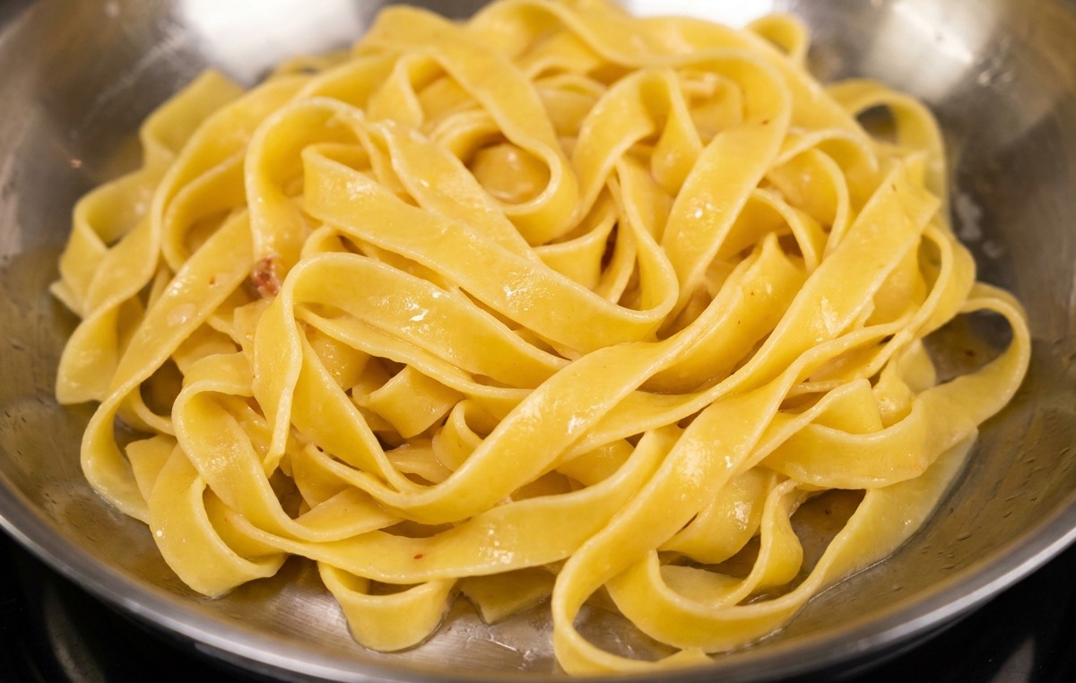 Makaron fettuccine dodawany na patelnię z wytopionym tłuszczem i kawałkami boczku.