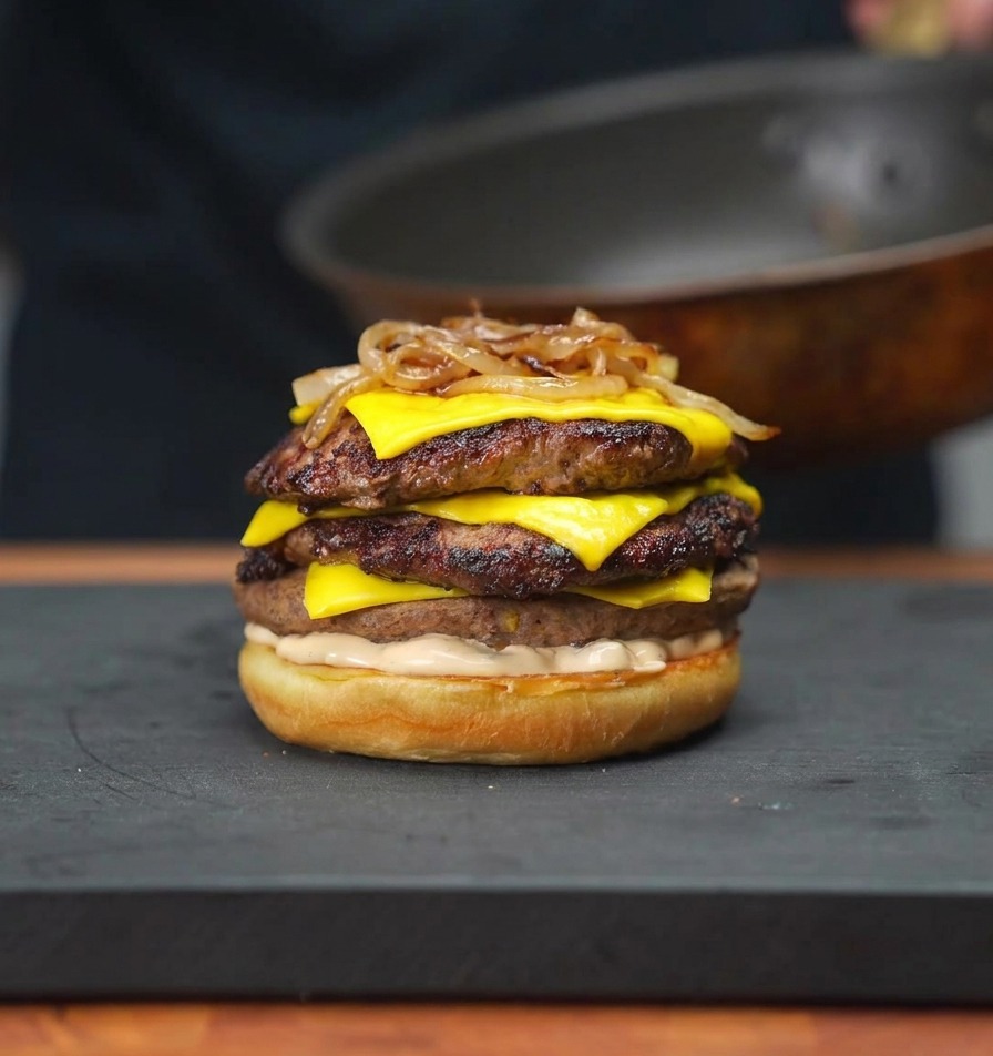 Karmelizowana cebula nakładana na górę burgera za pomocą pałeczek kuchennych.