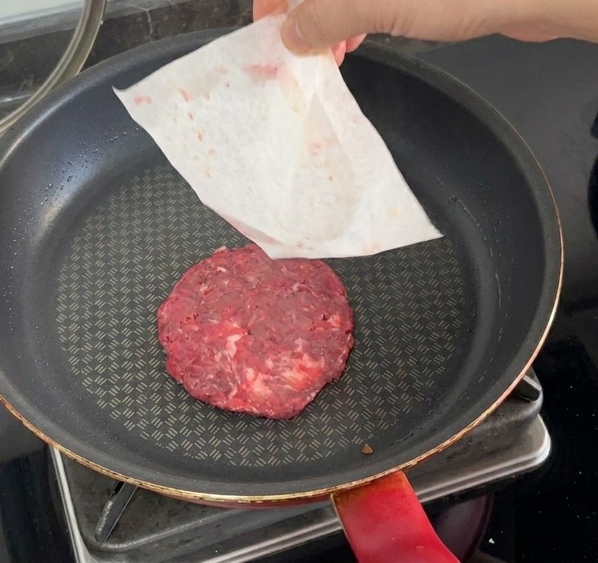 Surowy kotlet kładziony na gorącą patelnię przy jednoczesnym zdejmowaniu papieru.