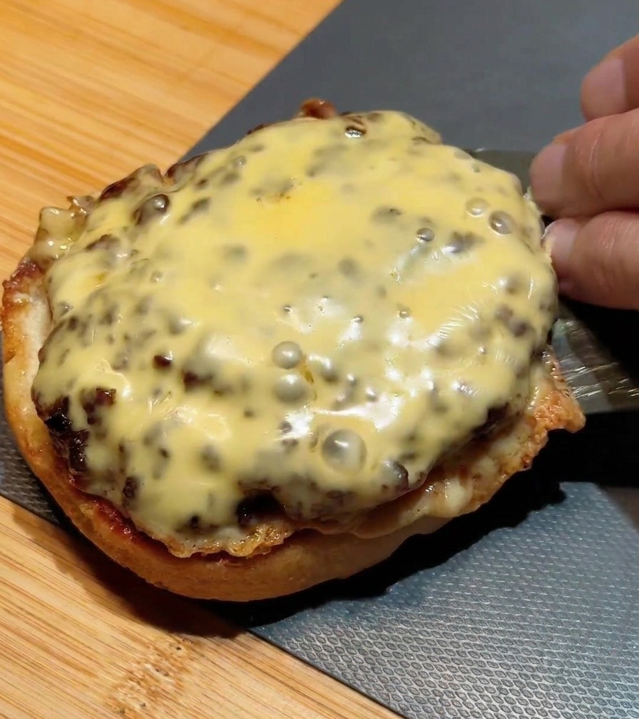 Metalowa łopatka kładąca drugi kotlet z serem na kotlet znajdujący się już na bułce.