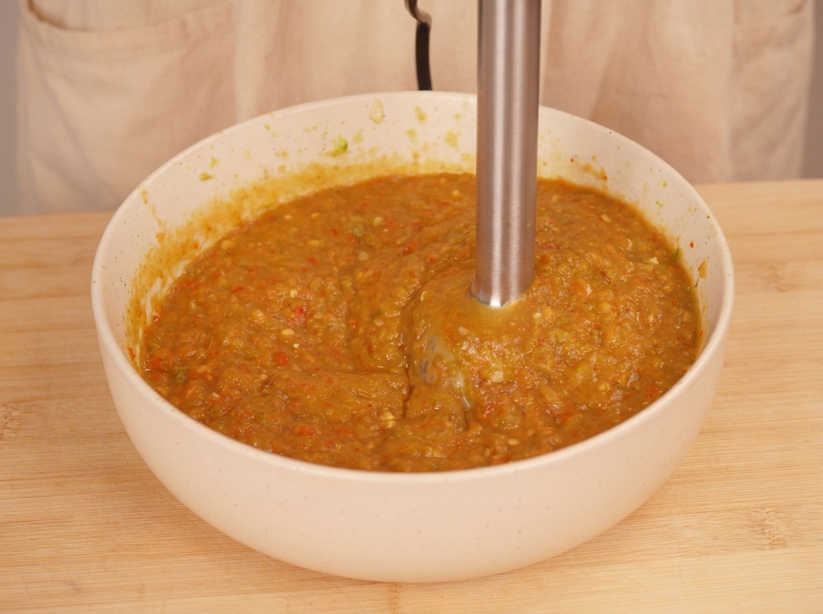 Blender ręczny miksujący pieczone warzywa na gęsty, pomarańczowo-zielony sos o wyraźnej strukturze.