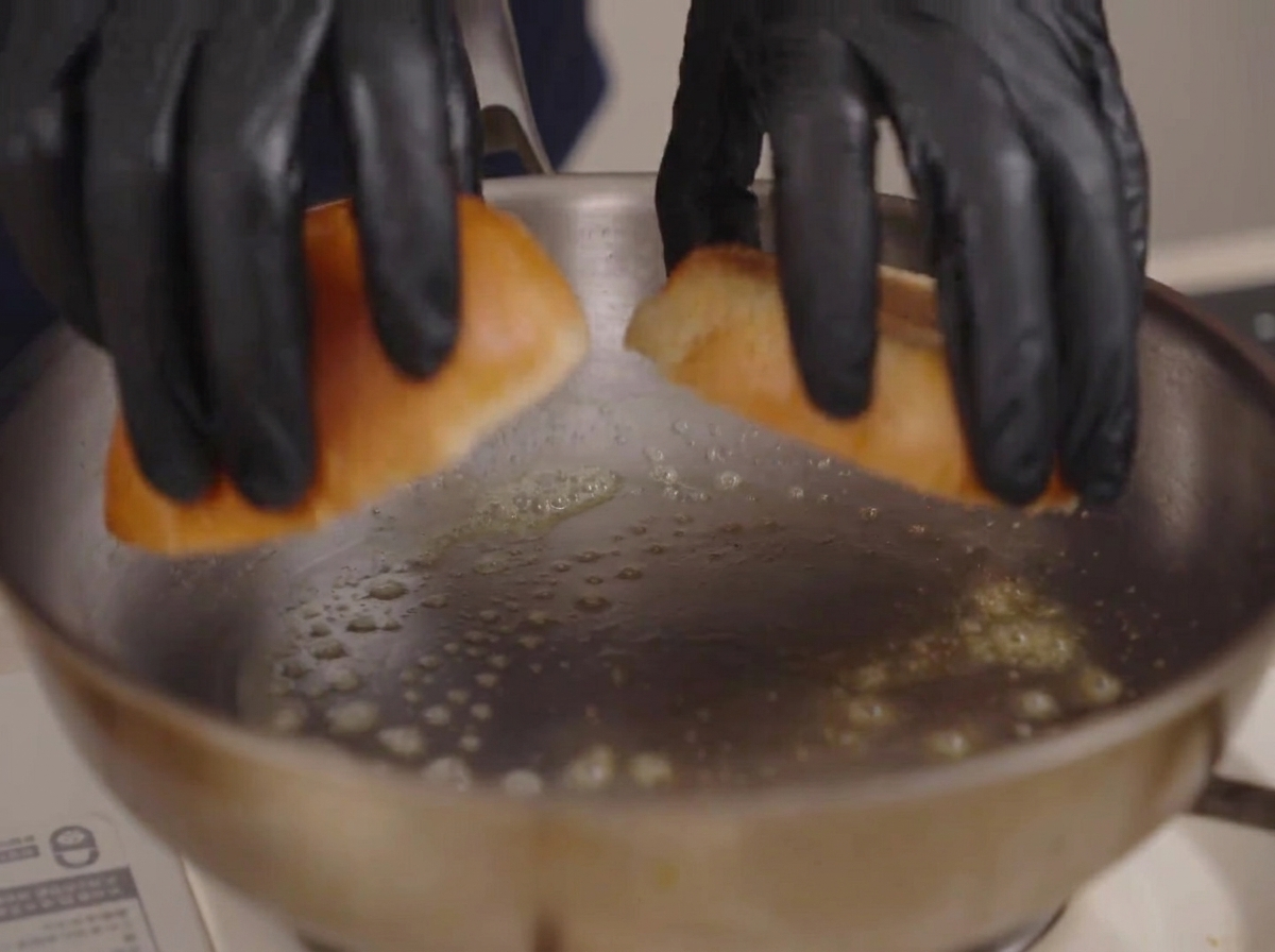 Ręce w rękawiczkach kładą połówki bułek brioche na patelnię z pieniącym się masłem.
