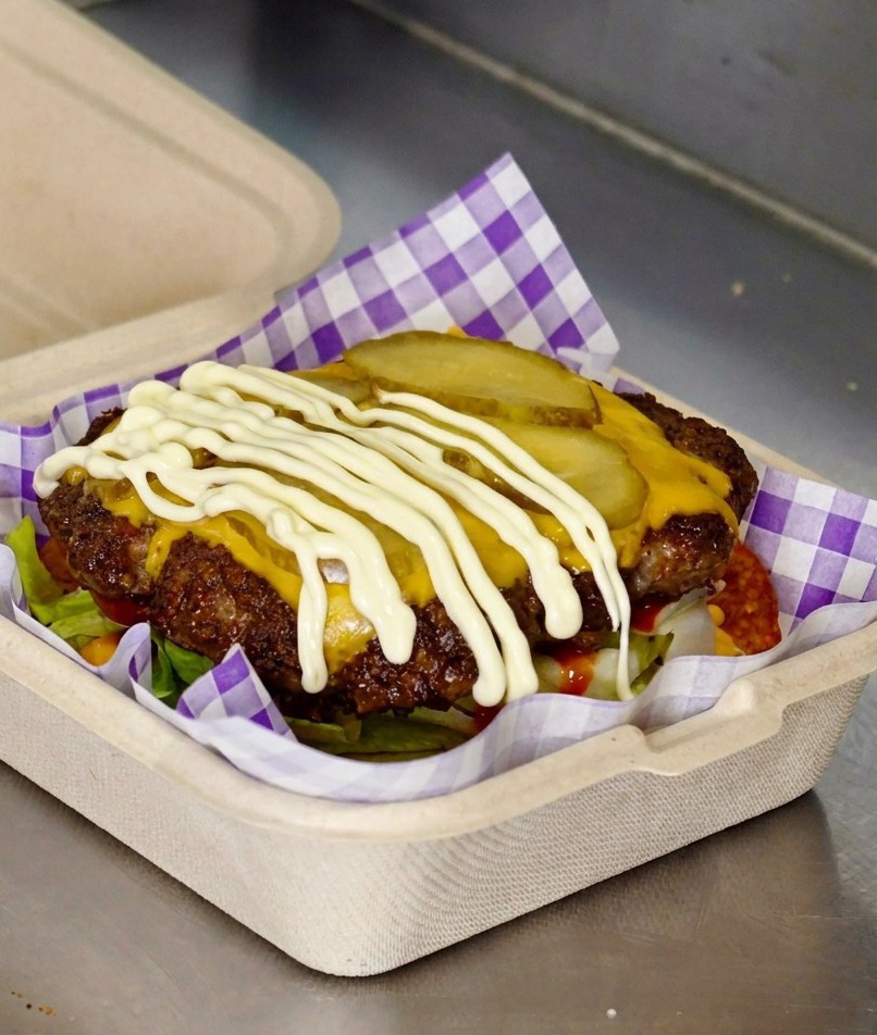 Biały majonez wyciskany na plasterki korniszonów na burgerze.