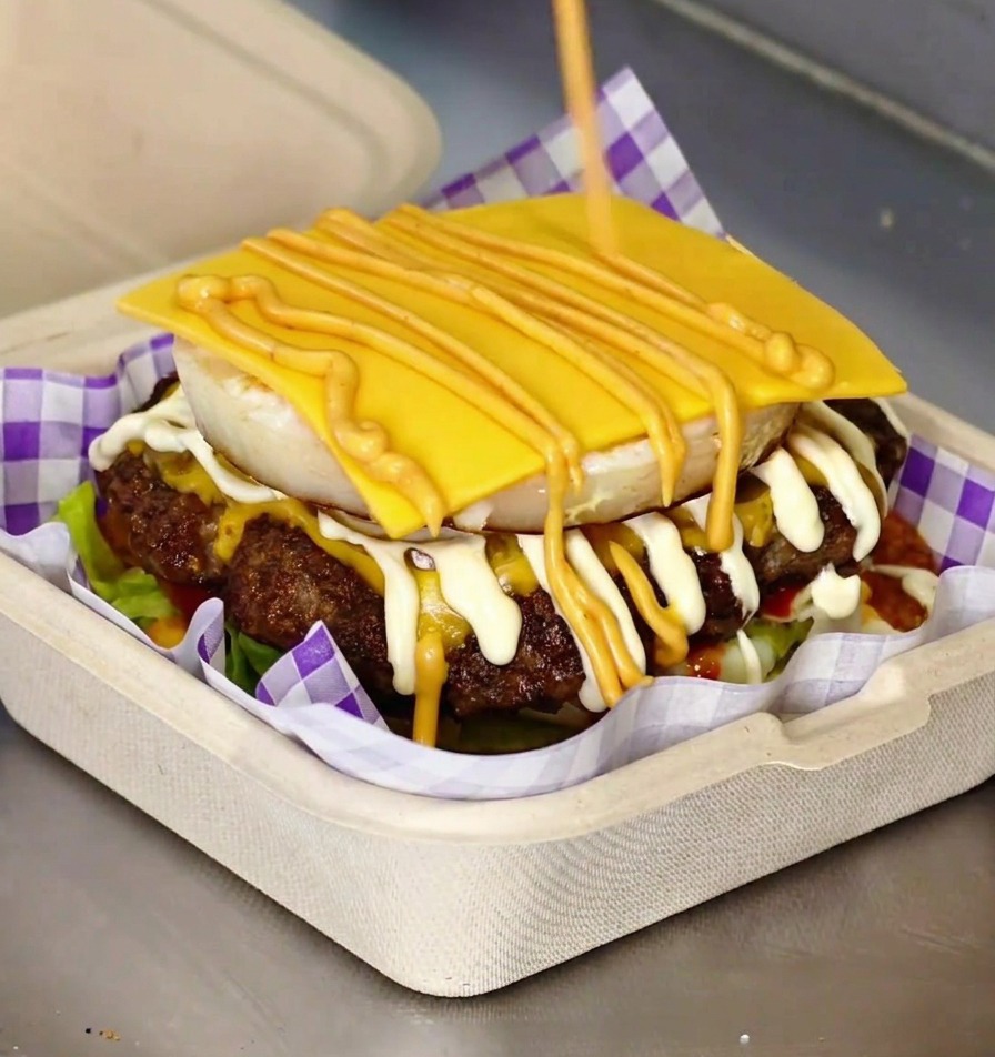 Gotowy burger gourmet z widocznym jajkiem i serem w bułce brioche.