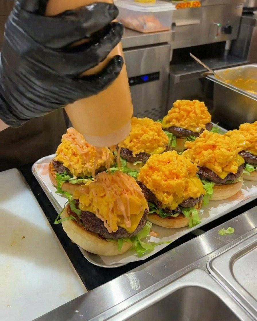 Pomarańczowy sos do burgerów wyciskany na stos jajecznicy w złożonym burgerze.