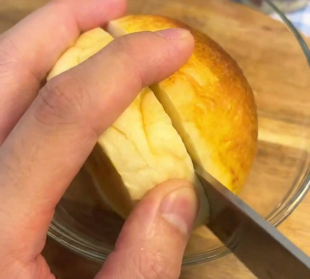 Nóż z ząbkami przekrawający na pół idealnie przypieczoną, złocistą bułkę brioche na drewnianym blacie.