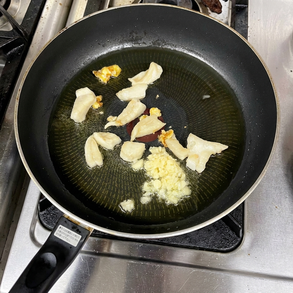 Posiekany czosnek i skwarki smażące się w klarownym oleju na patelni.