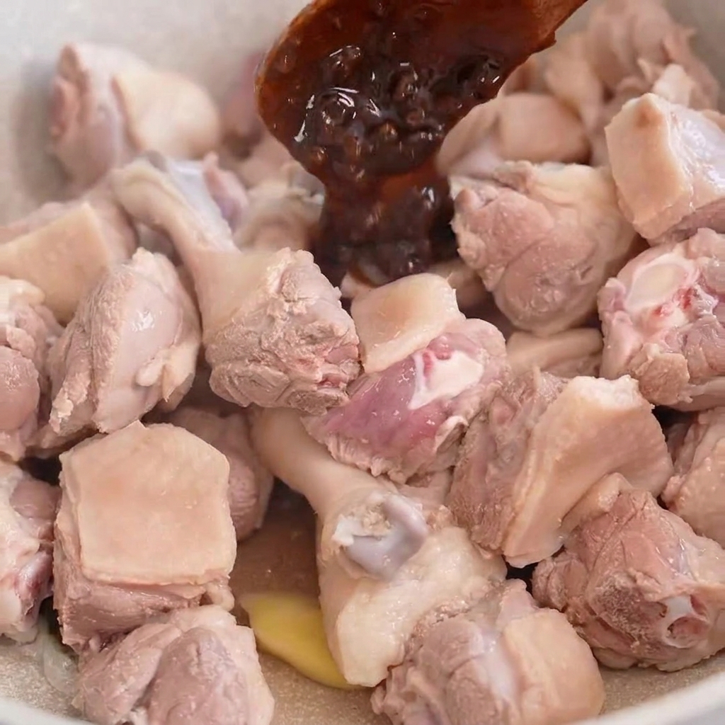 Drewniana łyżka nakładająca ciemną pastę fasolową na kawałki kaczki smażone na patelni.