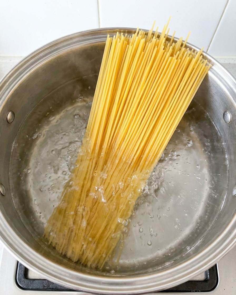 Makaron spaghetti gotujący się w dużym garnku z wrzącą wodą.