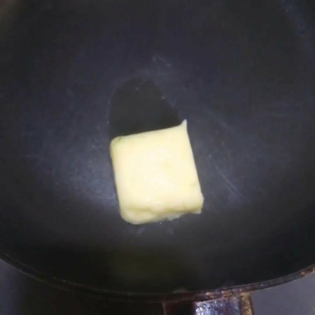 Kawałek masła roztapiający się i skwierczący na gorącej patelni.