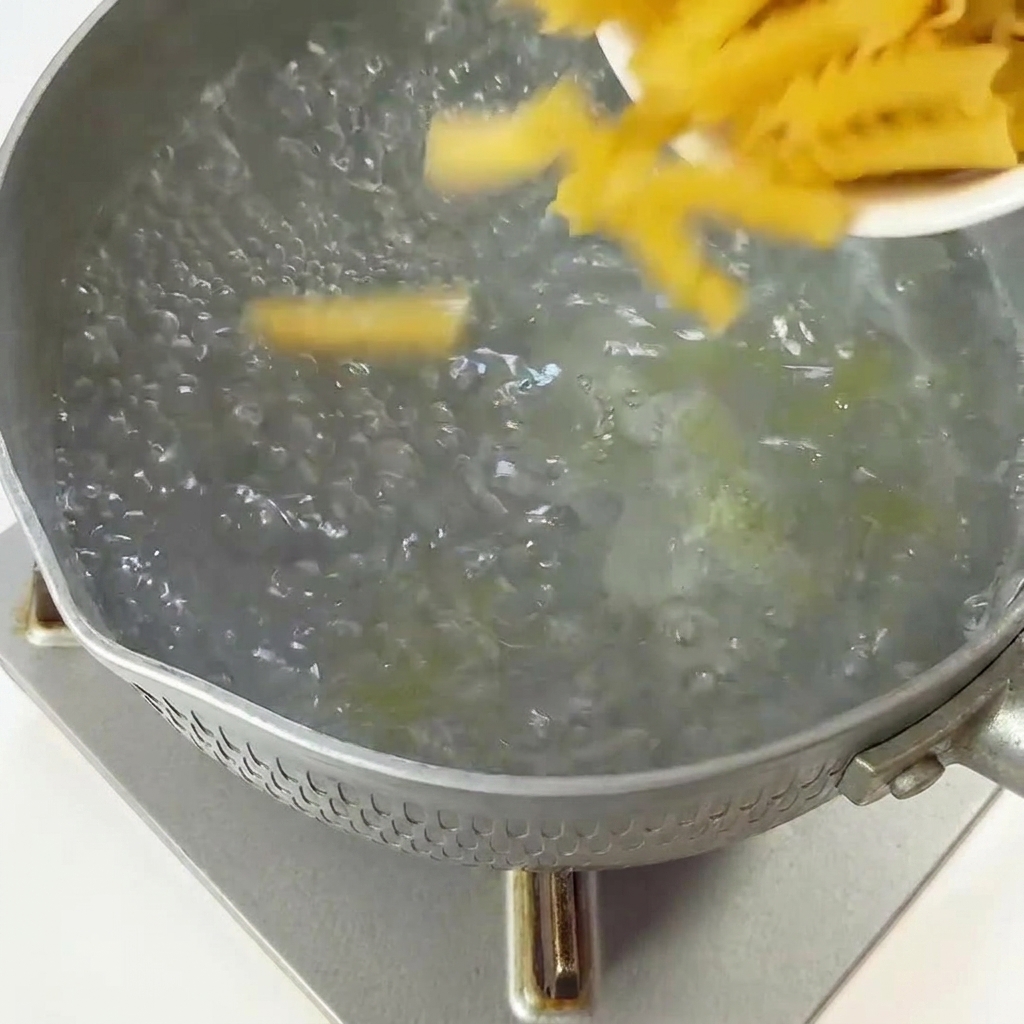 Surowy makaron fusilli wsypywany do garnka z wrzącą wodą.