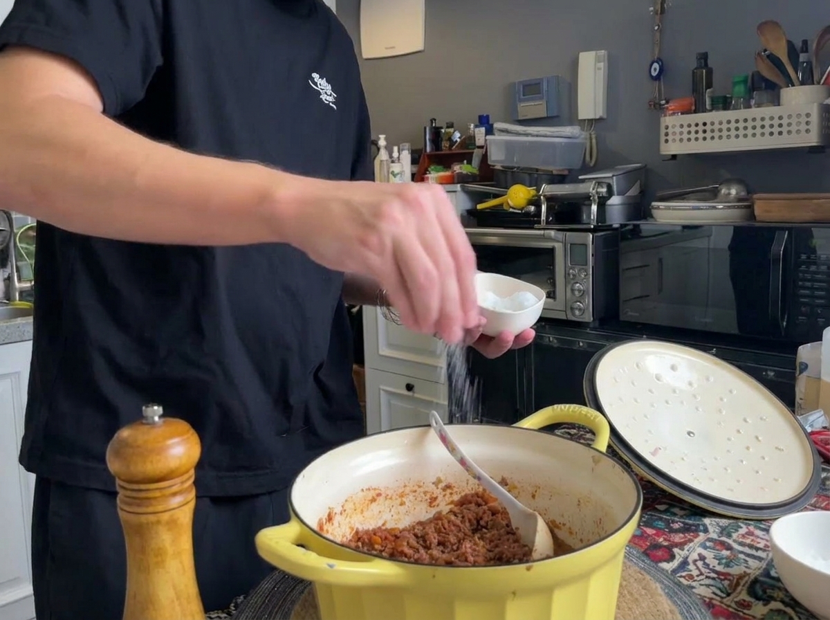 Świeżo mielony czarny pieprz i sól dodawane do garnka z gotowym ragù.