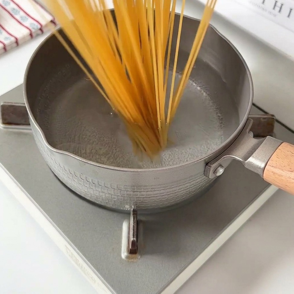 Nitki spaghetti wpadające do garnka z wrzącą wodą.