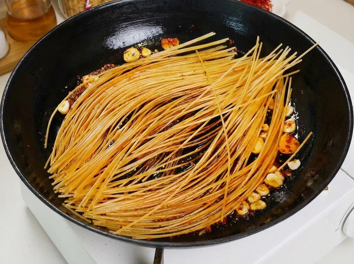 Chochla wlewająca czerwony bulion pomidorowy na podsmażane spaghetti na czarnej patelni.