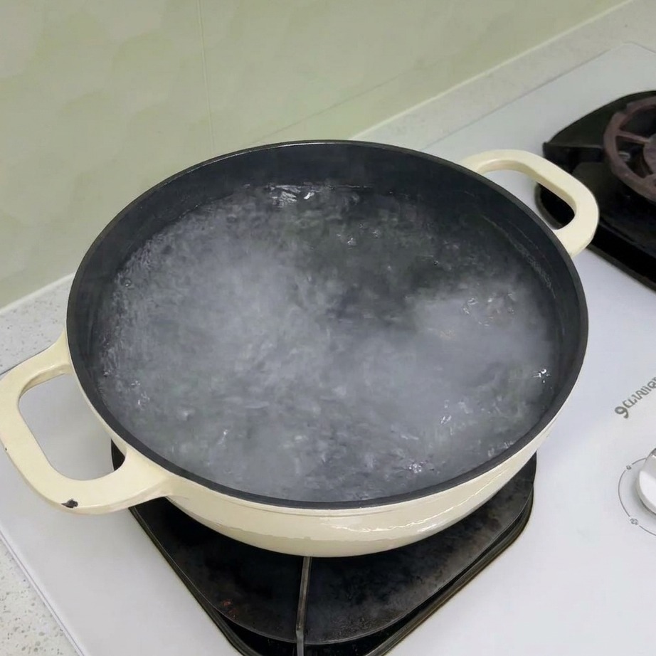 Suchy makaron rotini wrzucany do garnka z wrzącą wodą.