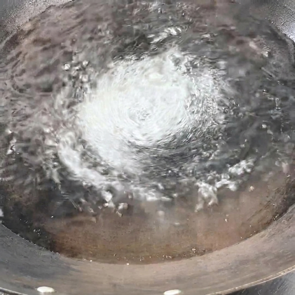 Wiązka suchego spaghetti wkładana pionowo do wrzącej wody w woku.