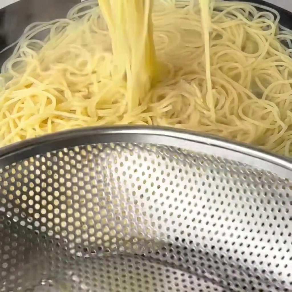 Ugotowane, miękkie nitki spaghetti wyjmowane z wody za pomocą długich drewnianych pałeczek.
