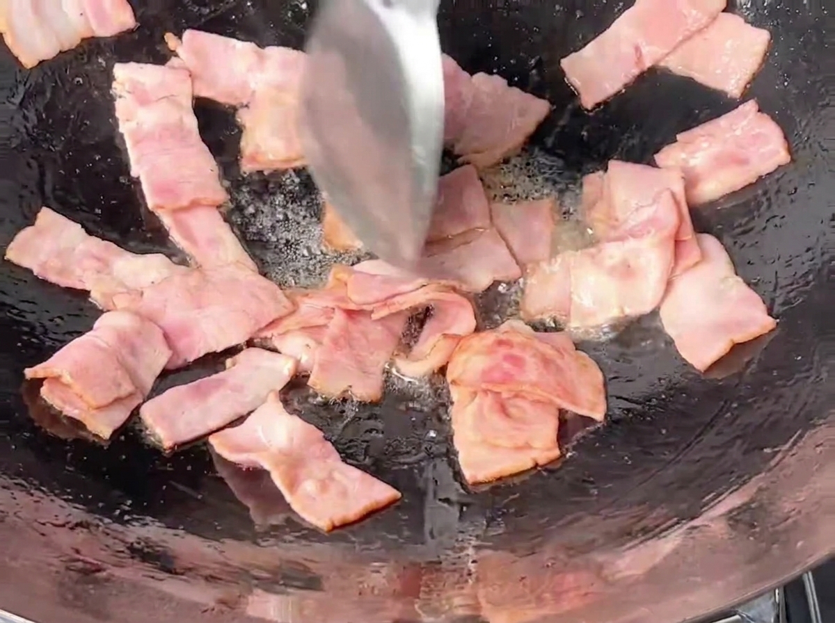 Kawałki boczku smażone w żelaznym woku przy użyciu metalowej łopatki.