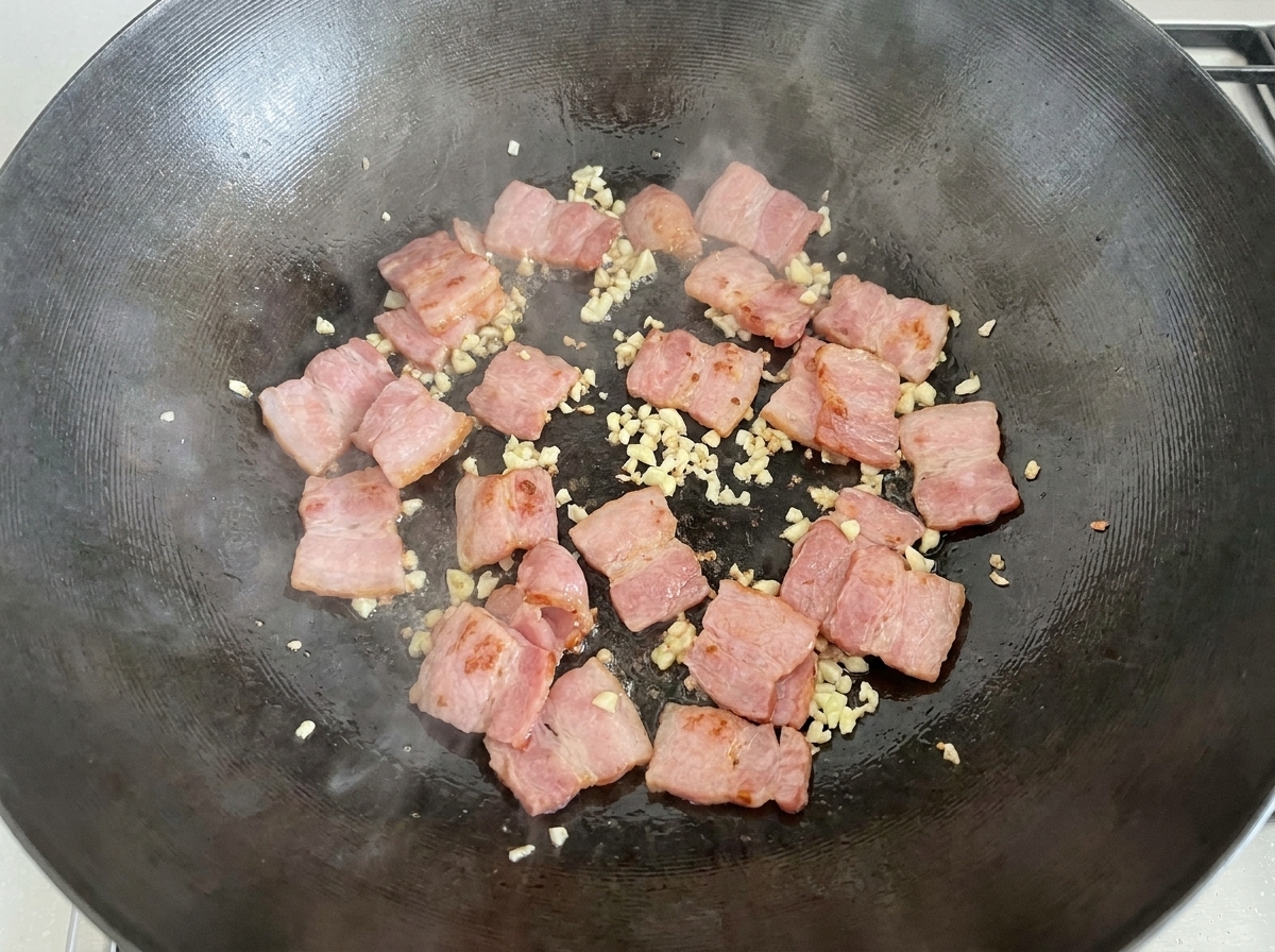Pokrojone pieczarki wsypywane do woka z boczkiem i czosnkiem.