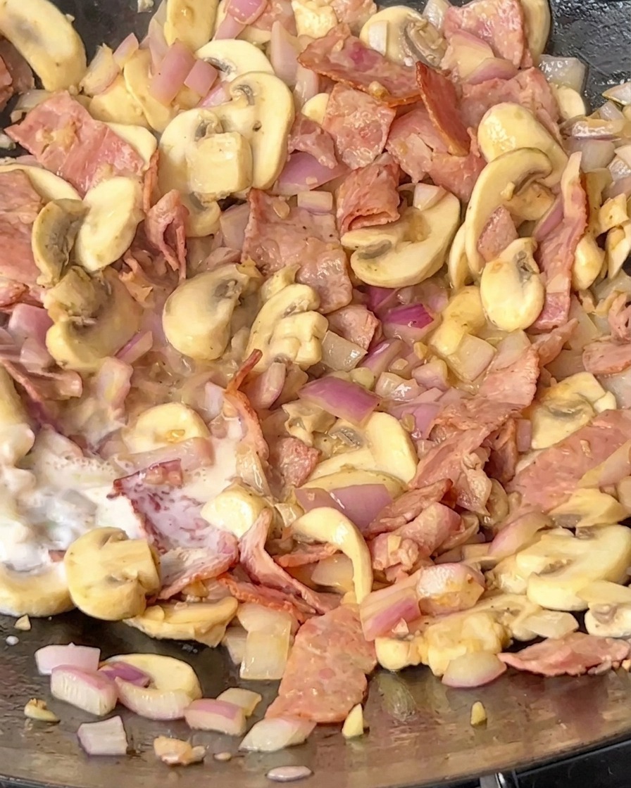 Mleko wlewane do woka z podsmażonym boczkiem, pieczarkami i cebulą.