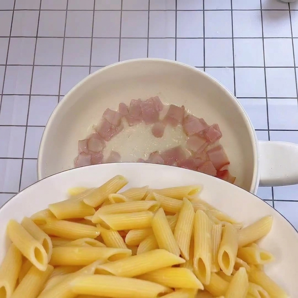 Świeżo ugotowane penne dodawane na patelnię z chrupiącymi kawałkami boczku.
