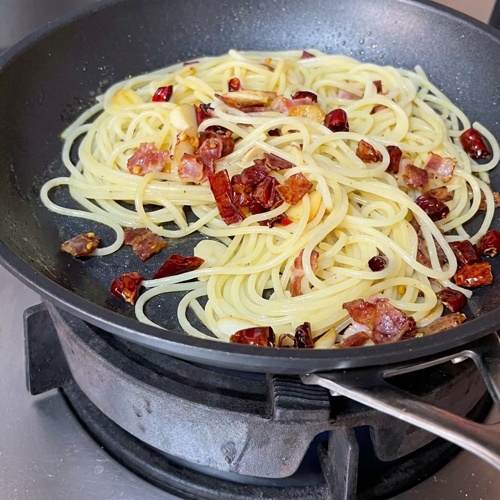 Spaghetti, bekon i aromaty mieszane łopatką na patelni.