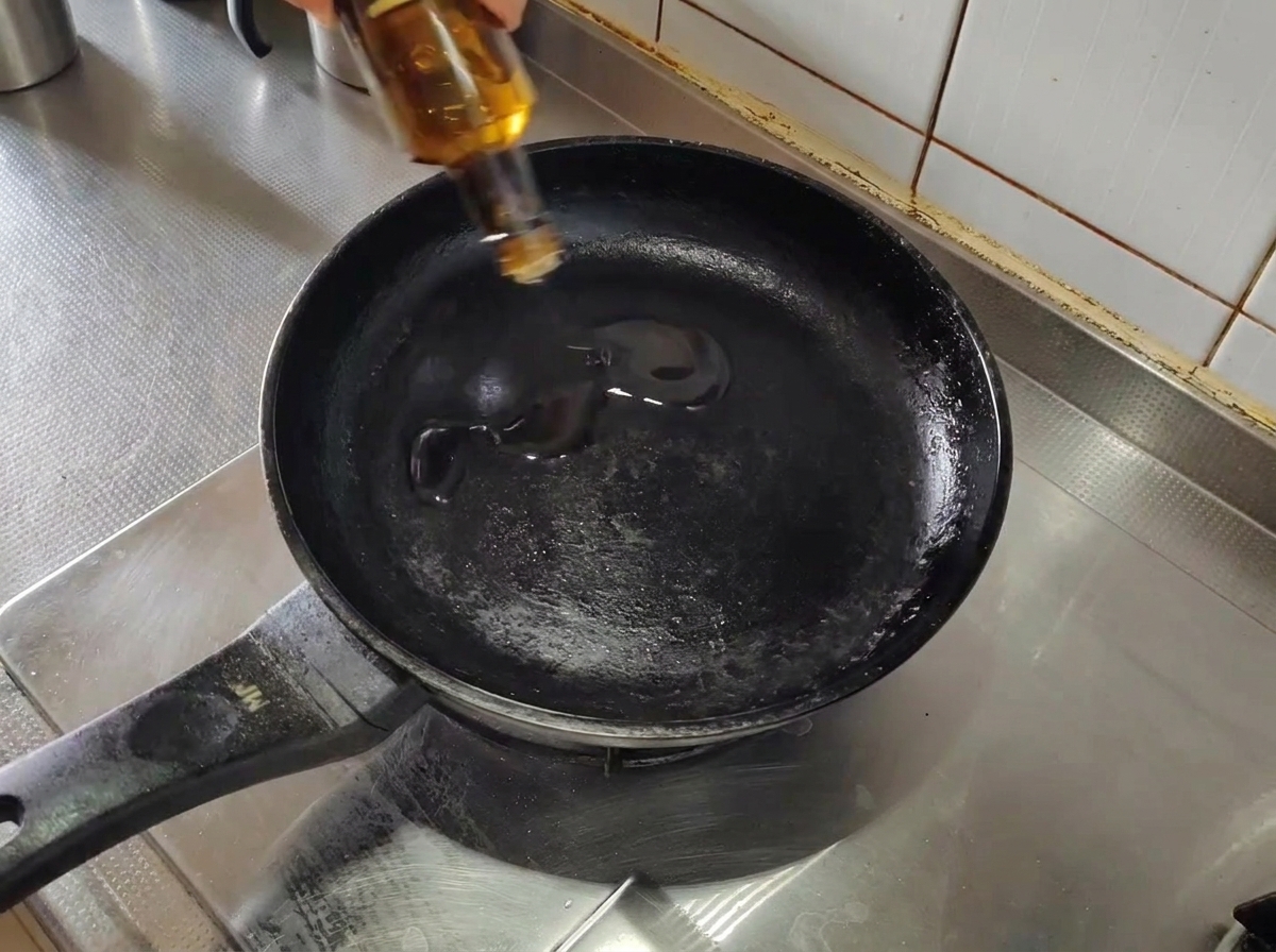 Oliwa wlewana do pustej, rozgrzanej czarnej patelni na kuchence.