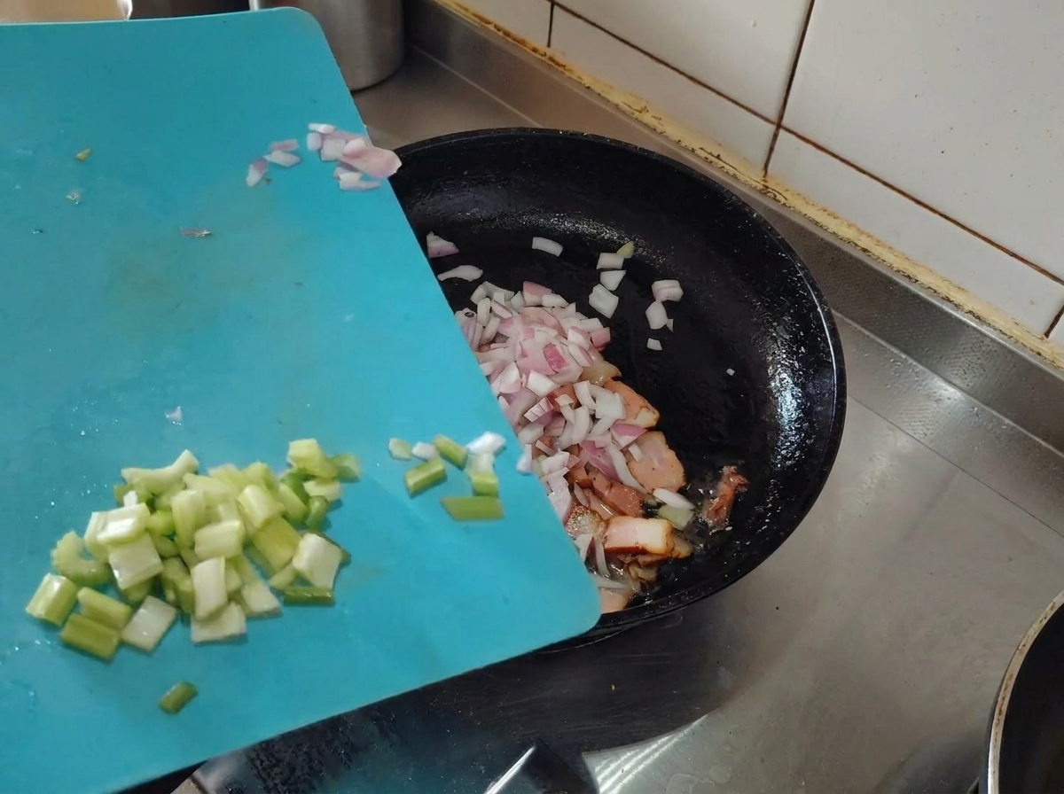 Posiekana szalotka i seler naciowy dodawane na patelnię z zarumienionym boczkiem.
