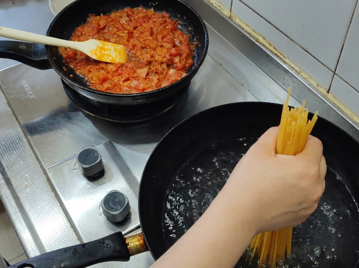 Garść surowego makaronu spaghetti zanurzana w garnku z gotującą się wodą.